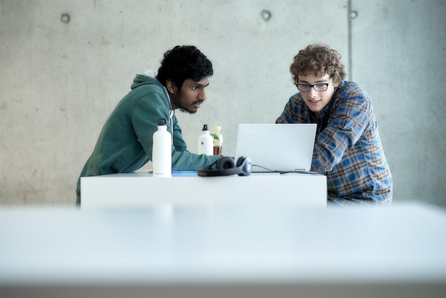 Zwei Studenten in legerer Kleidung arbeiten gemeinsam konzentriert an einem aufgeklappten Laptop-Computer.