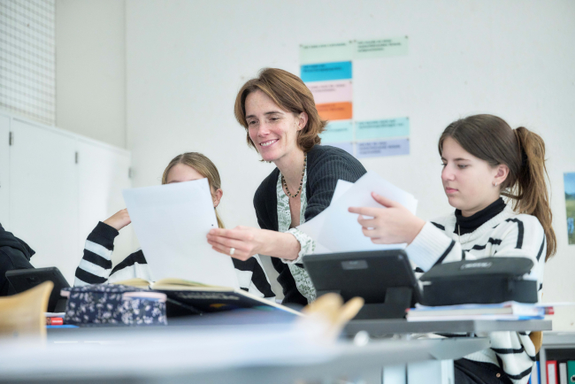 Lächelnde Lehrerin bespricht Arbeisblätter mit zwei Schülerinnen